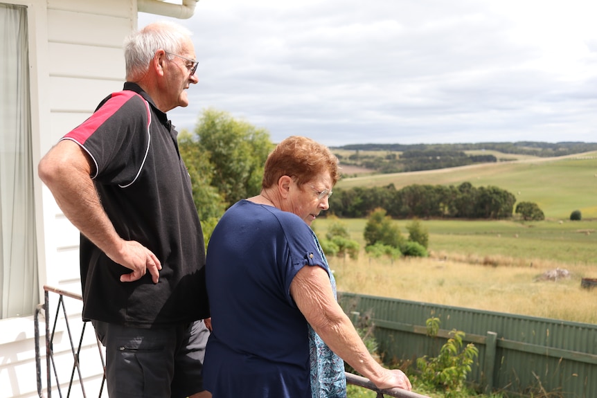 A man and woman of retirement age stand on balcony looking out to farmland.