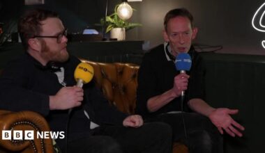 Huw Stephens and Steve Lamacq sit on a sofa at the venue holding 6 Music microphones.