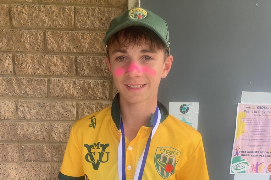 A teenage boy smiling and holding a cricket trophy.