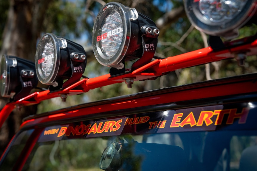 Large flashlights fixed on top of a vehicle. Underneath a sticker reads when Dinosaurs ruled the Earth