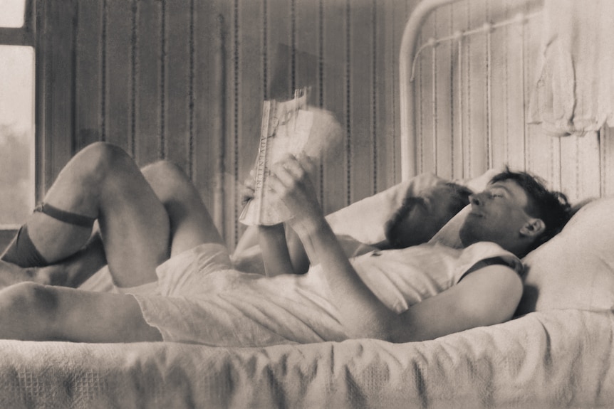 Two men lying on a bed reading.