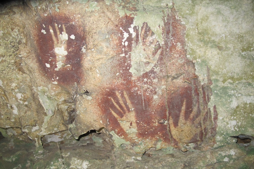 A rock wall with the inverted print of four hands, sprayed with red ochre.