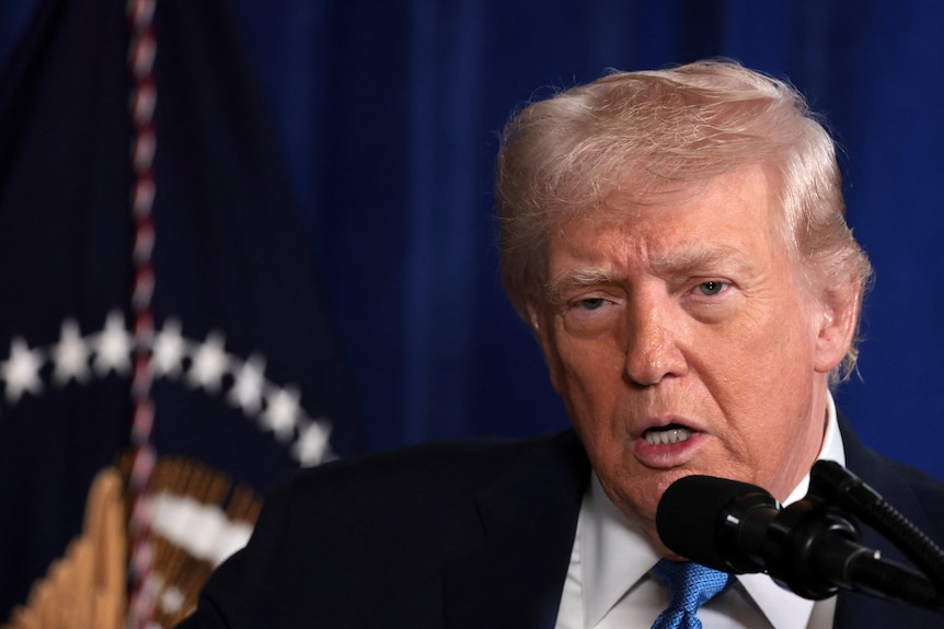 Donald Trump speaks into a microphone at a press conference.