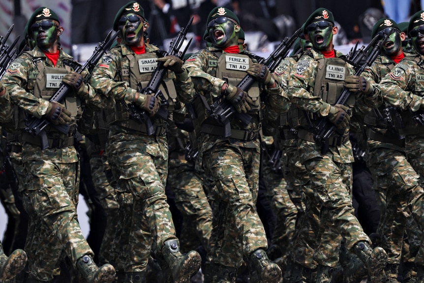 Five men wearing army uniforms and face painted walking in a line.