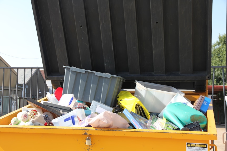 A yellow rubbish bin overflows with rubbish