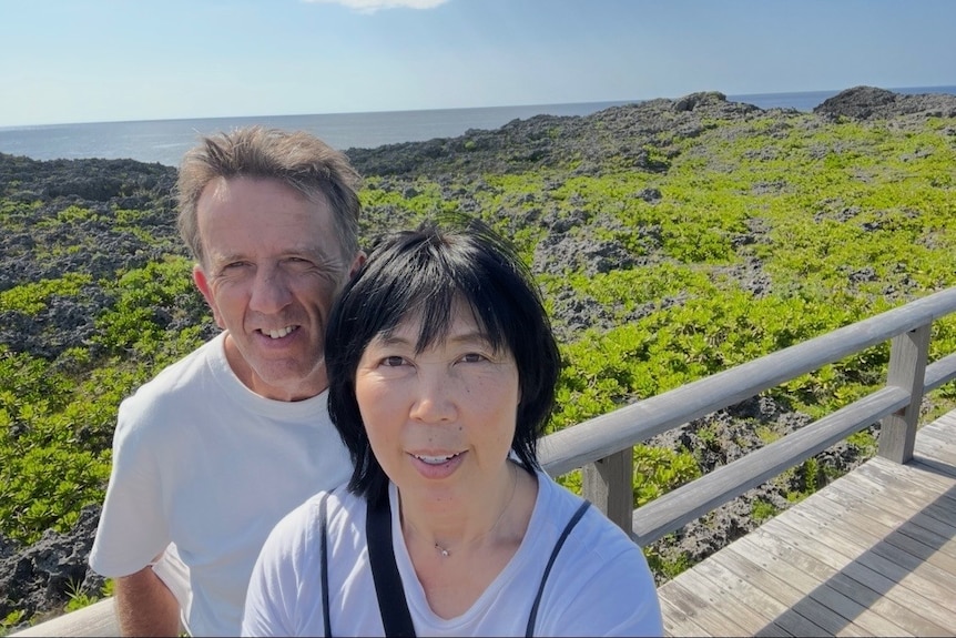 A man and a woman take a selfie on a coastal boardwalk.