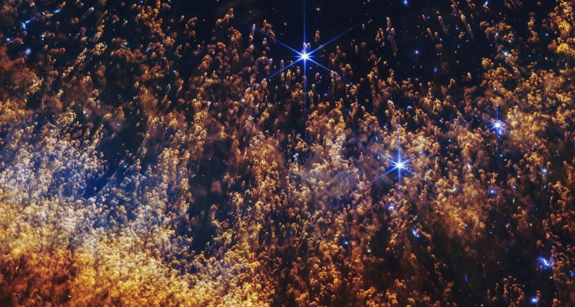 Hundreds of gold and orange clouds with feathered trails going down behind them. The small clouds are covering a few scattered, bright stars.