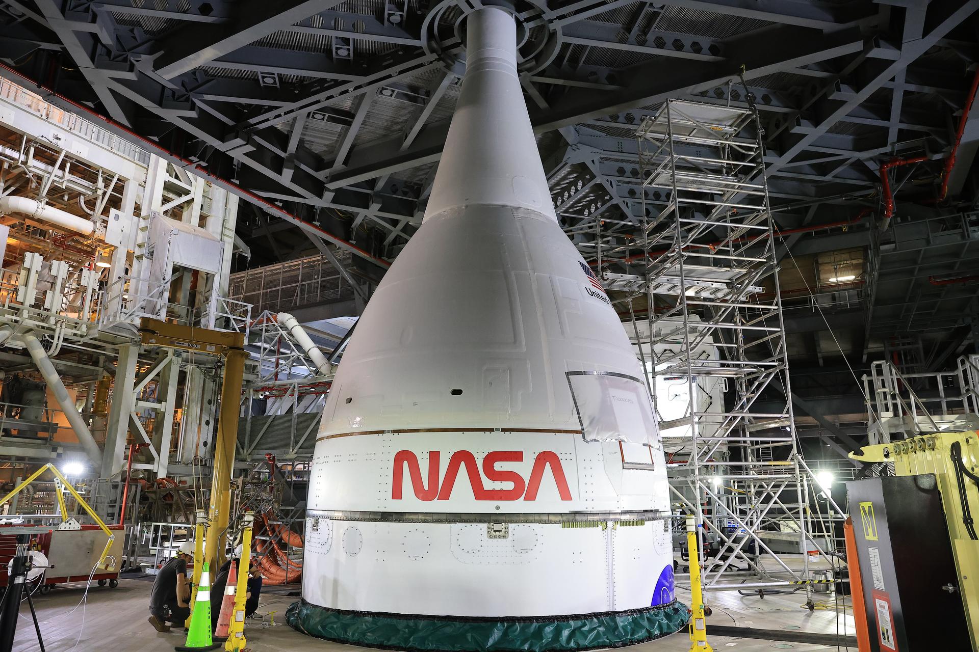 A white rocket nose and top half of the body sit in a warehouse surrounded by scaffolding.