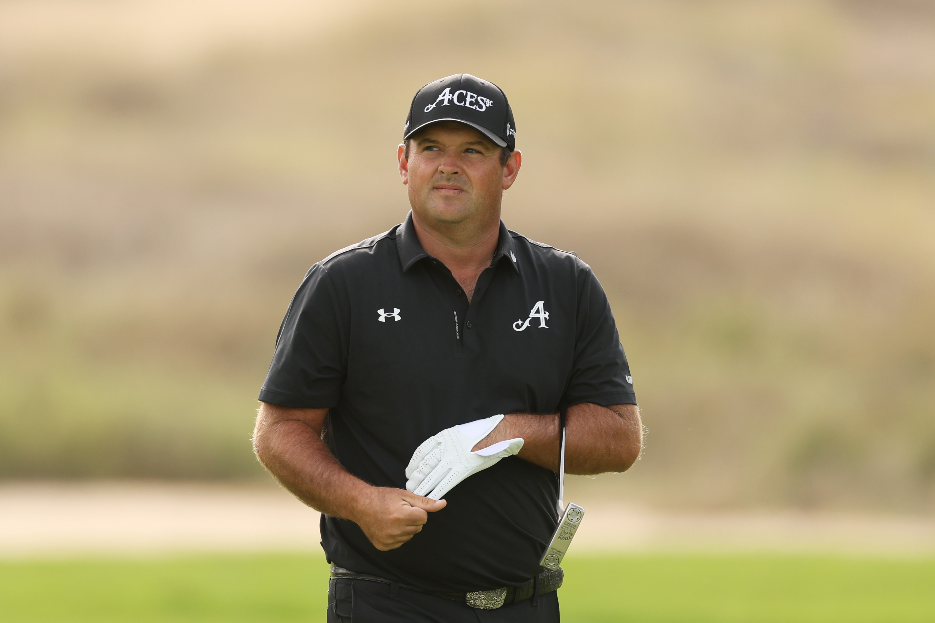 Patrick Reed removes his glove as he walks on the green