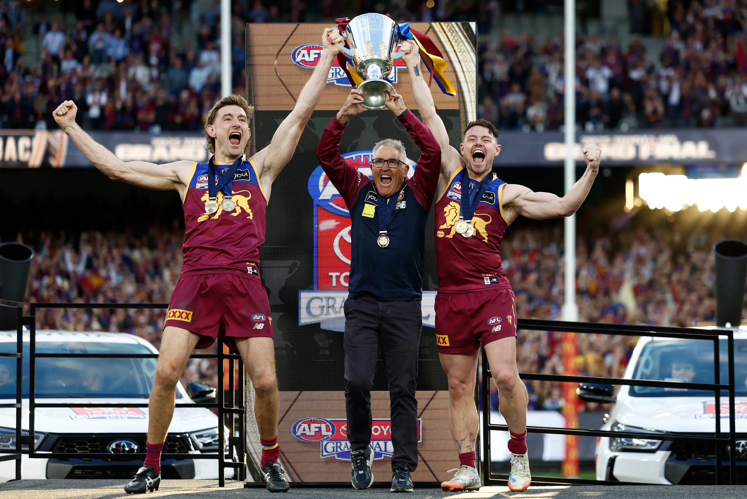 MELBOURNE, AUSTRALIA - SEPTEMBER 27: Harris Andrews of the Lions, Chris Fagan, Senior Coach of the Lions and Lachie Neale of the Lions celebrate with the Premiership Cup on the dais during the AFL Grand Final match between the Geelong Cats and the Brisbane Lions at the Melbourne Cricket Ground on September 27, 2025 in Melbourne, Australia. (Photo by Michael Willson/AFL Photos via Getty Images)