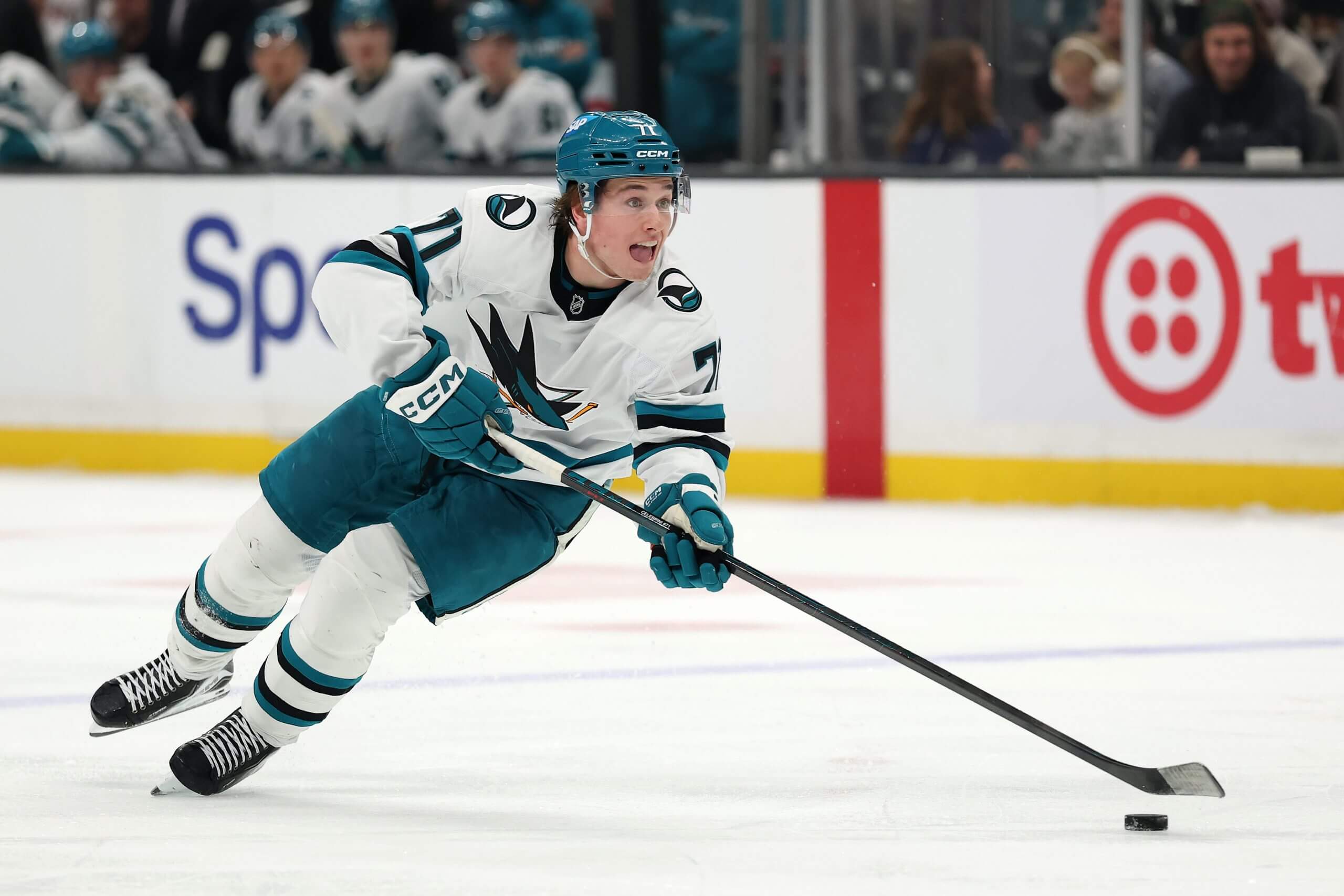 Macklin Celebrini skates with the puck, his tongue hanging slightly out.