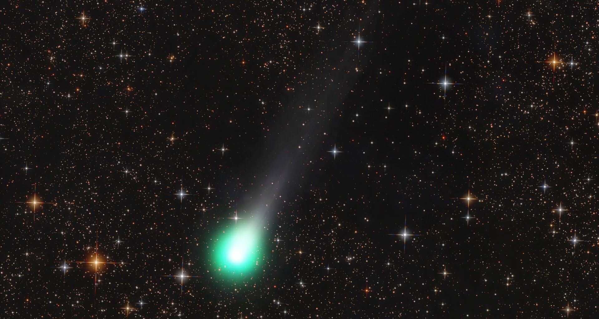 A green ball of light showing comet Lemmon streaks across an orange and black night sky full of stars.