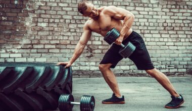 Man leaning against a tyre with one hand and performing a dumbbell bentover row with his left arm