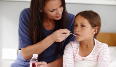 Mother holding a bottle of medicine. Mother giving sick young daughter a spoon of antibiotic medicine. Daughter is in bed.