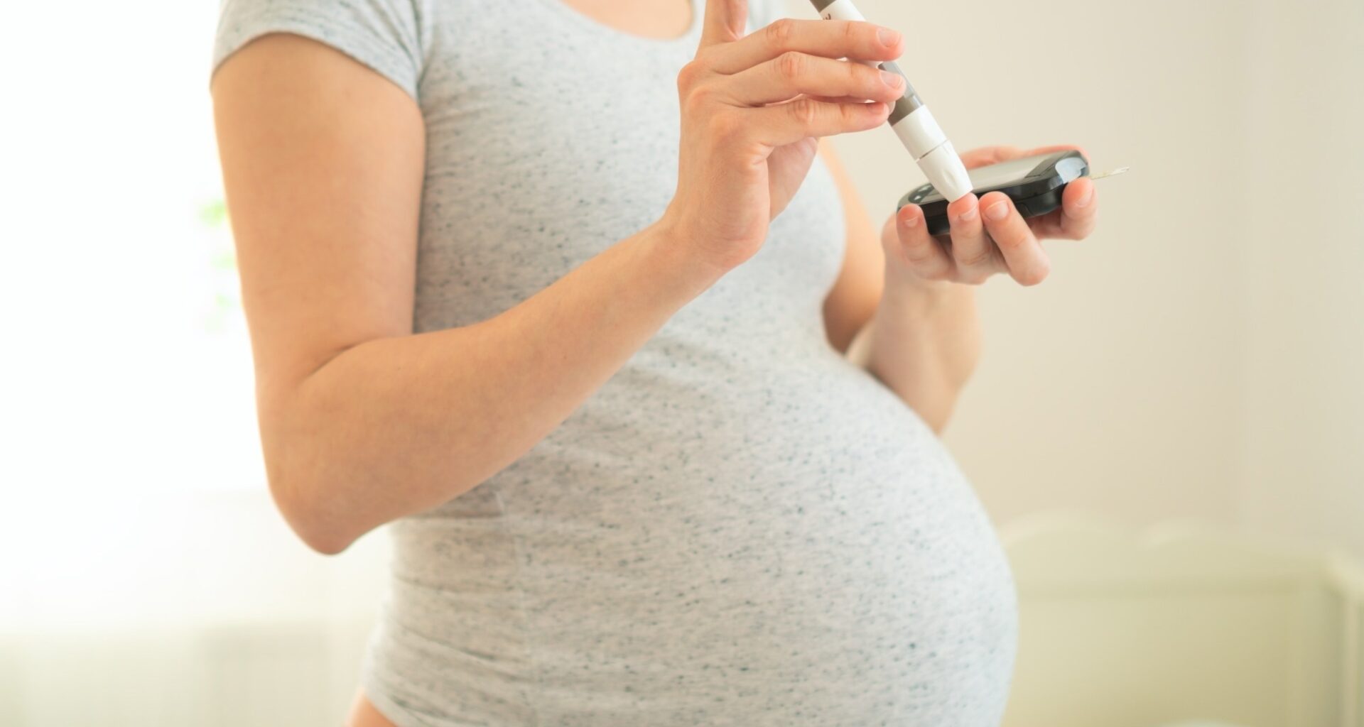 Pregnant woman using a blood glucose meter. Close-up of hands holding a glucometer and test strip.