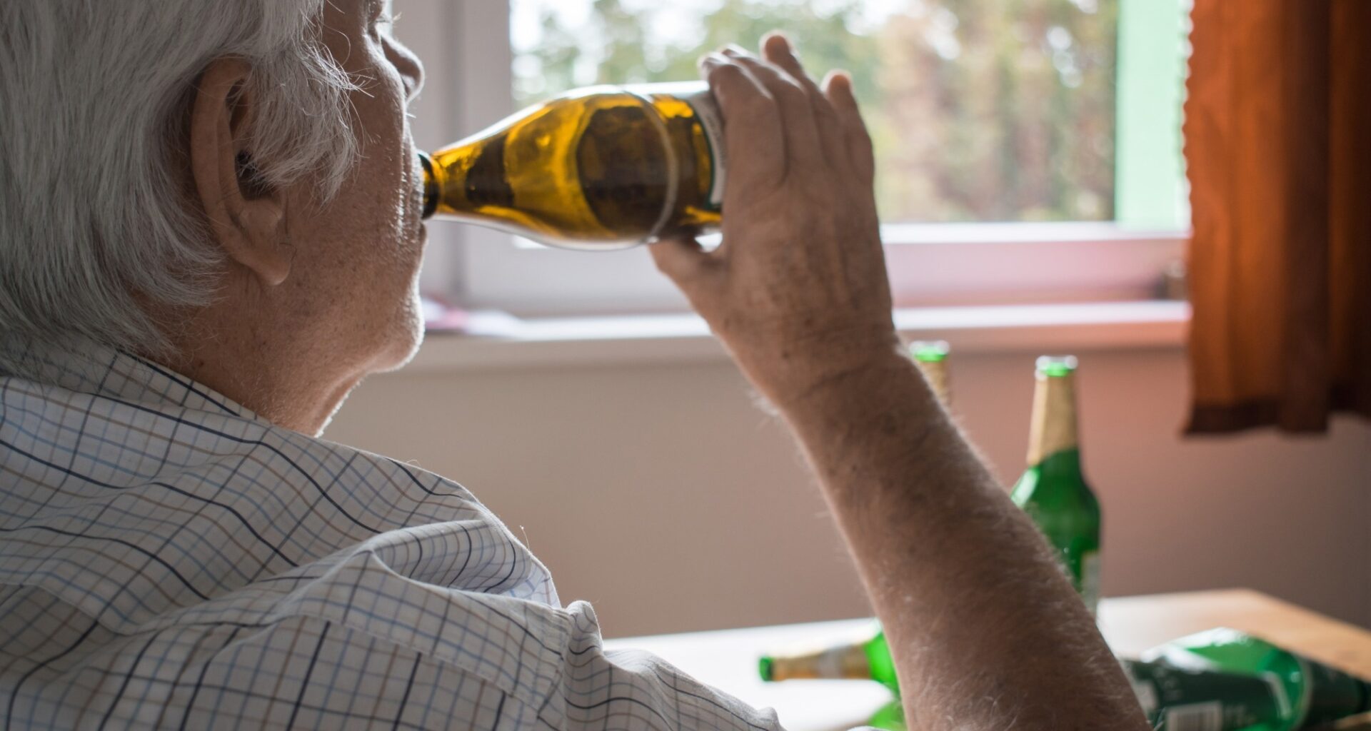 old senior man sit next to table drink alcohol bottle at home