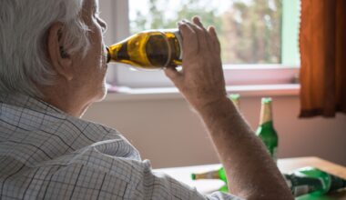 old senior man sit next to table drink alcohol bottle at home