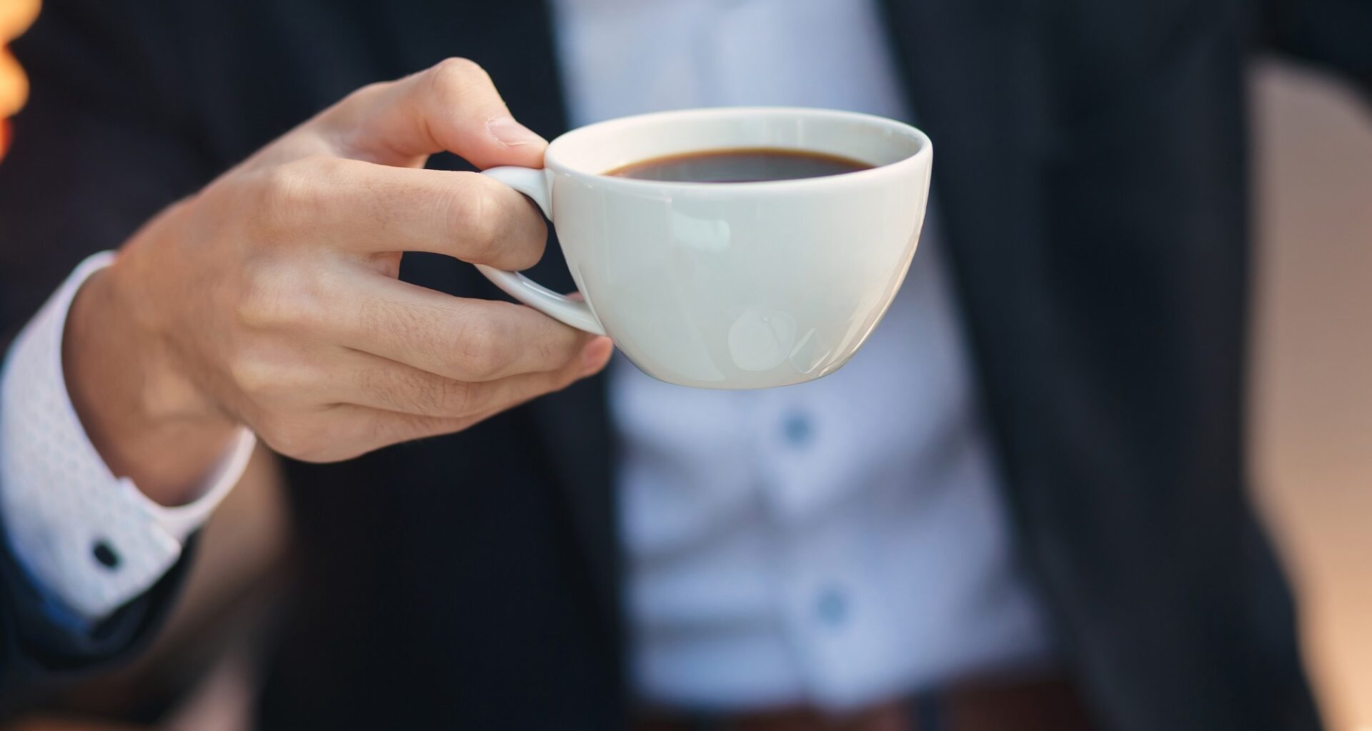 Close-up hand of young businessman in formal wear holding cup, mug of coffee