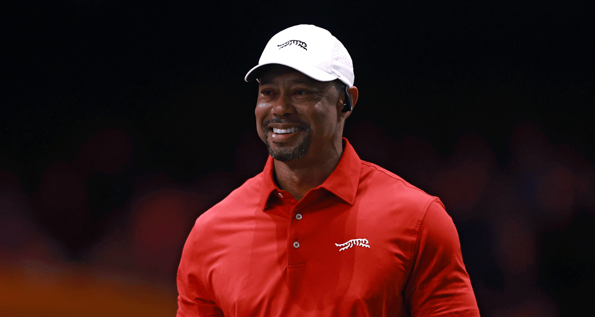 Tiger Woods smiles while wearing a white Sun Day Red cap and a red Sun Day Red polo during a TGL match in 2025