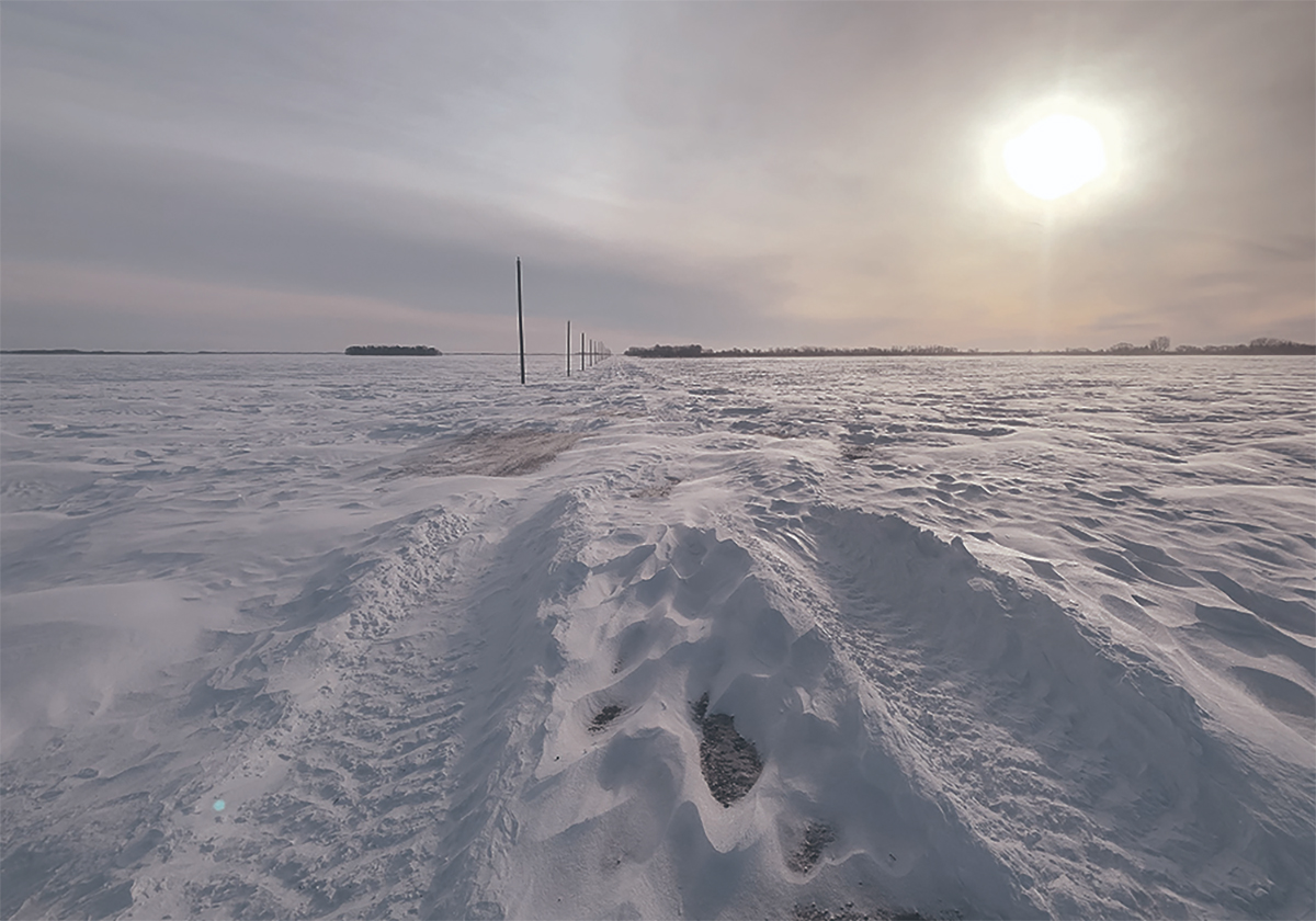 Looking down a country grid road clogged with snow as a winter storm is just coming to an end.