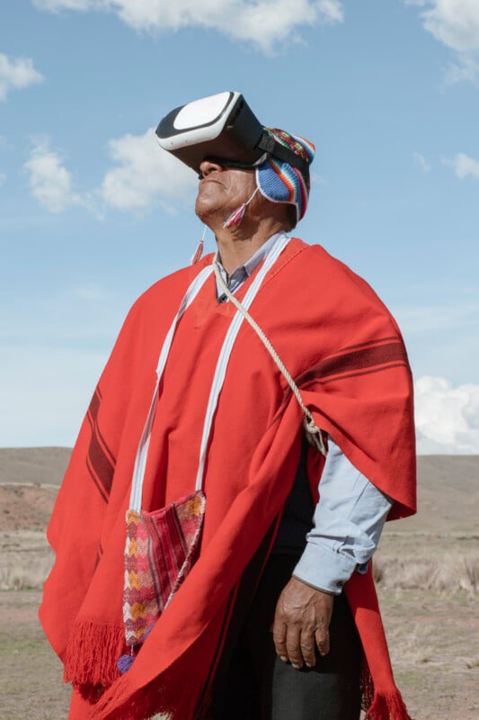 A person wearing traditional Andean clothing and a colorful hat uses a virtual reality headset outdoors, standing against a bright sky and natural landscape.