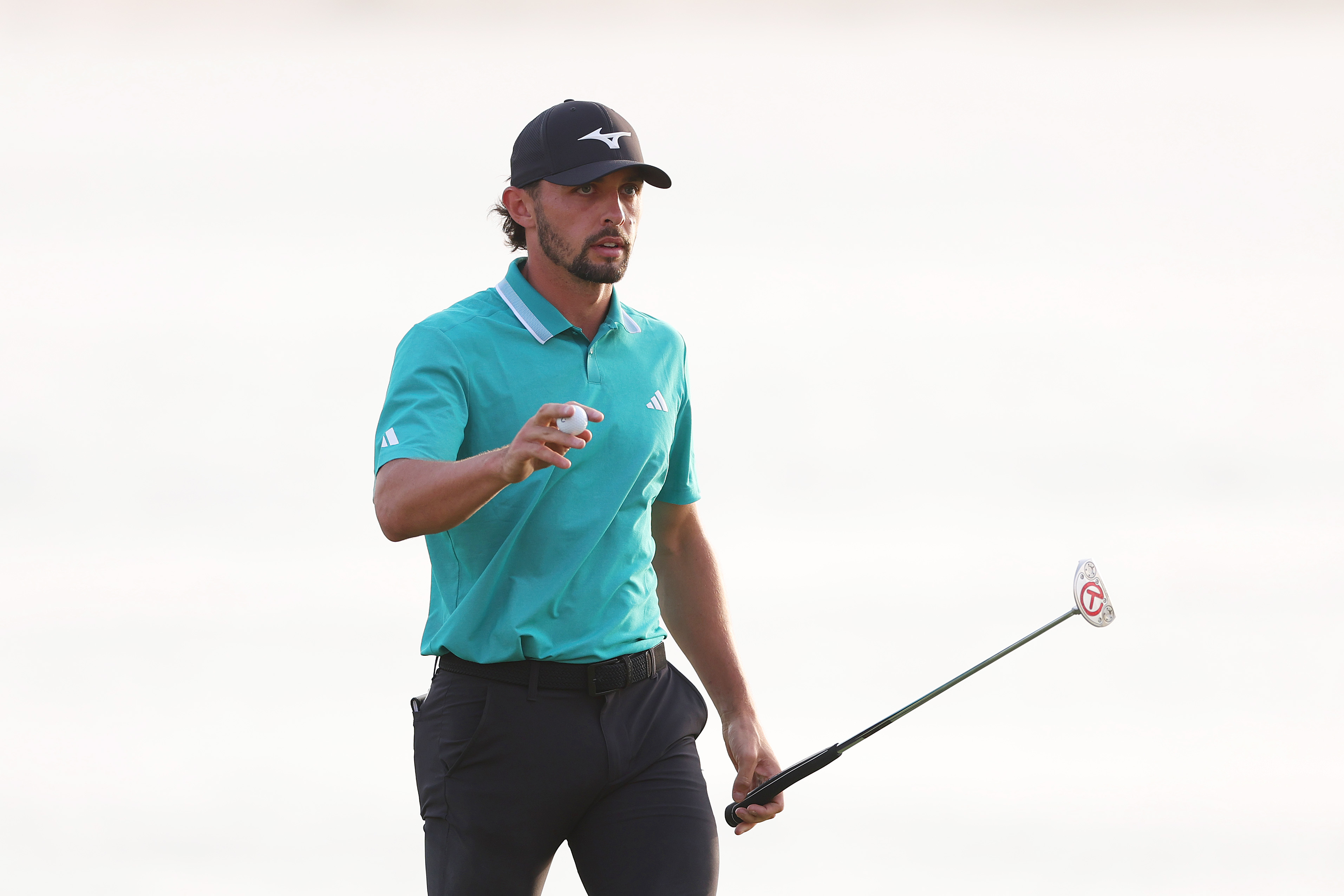 Marco Penge lifts his putter in the air while walking off the green