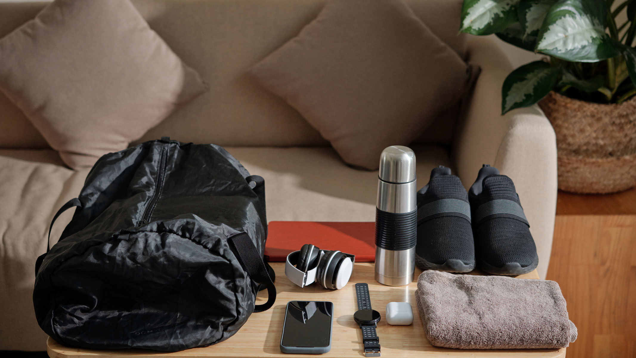 A picture of gym essentials - a gym bag, a water bottle, a fitness watch, a pair of headphones, a towel and a pair of running shoes - laid out on a table