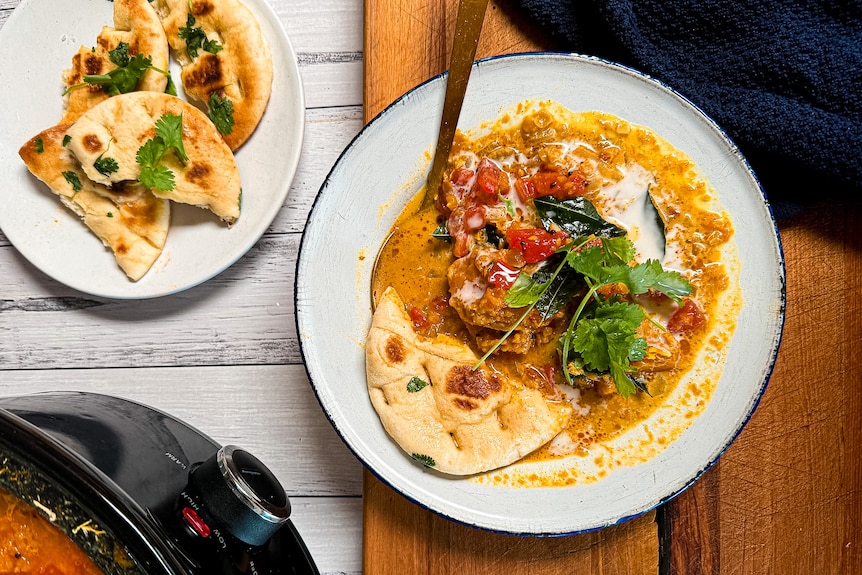 A plate of pumpkin, lentil and coconut curry, topped with coconut cream and tadka. Slow cooker visible with more curry.