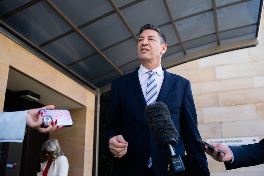 Basil Zempilas speaks in front of a microphone outside a building.