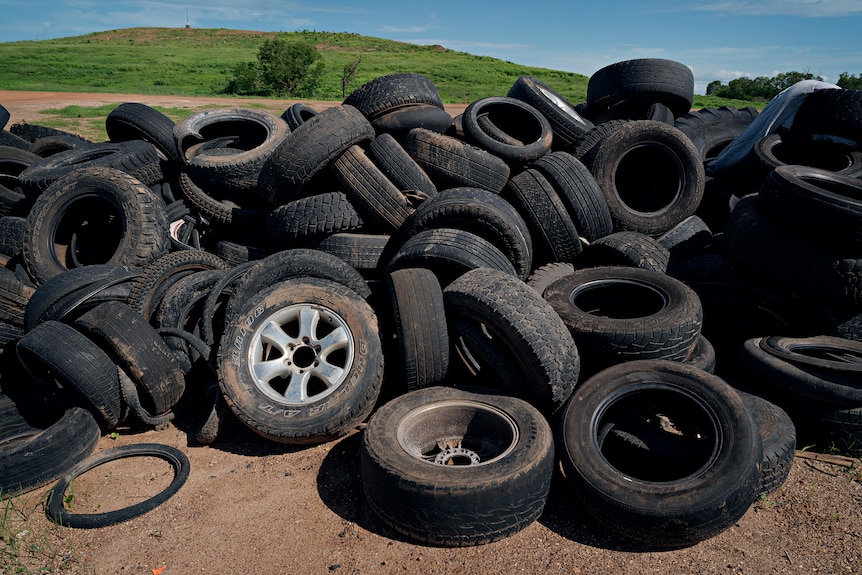 A pile of old tyres sitting on red dirt, a small grassy hill is visible in the background.