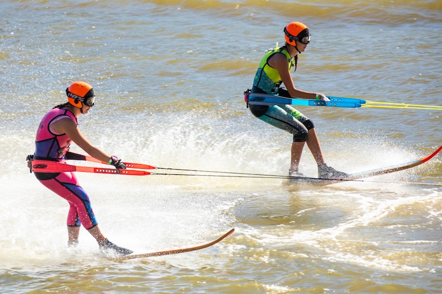 Two water skiers, one wearing a pink wetsuit, the other a lime green and blue wetsuit.