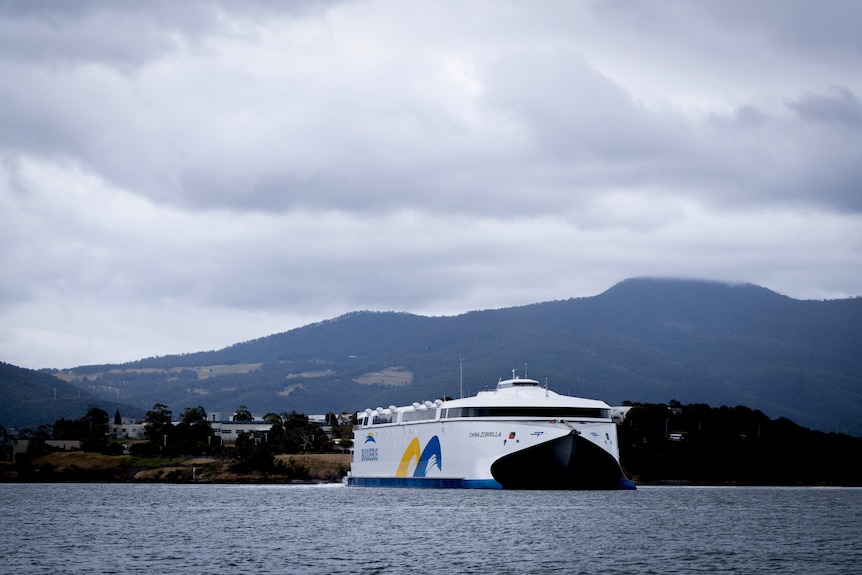 A large white ship pictured on a river in Hobart with mountains in the background. 
