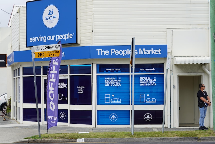 The facade of a building with bright blue signage and a plain-clothes police officer out the front.
