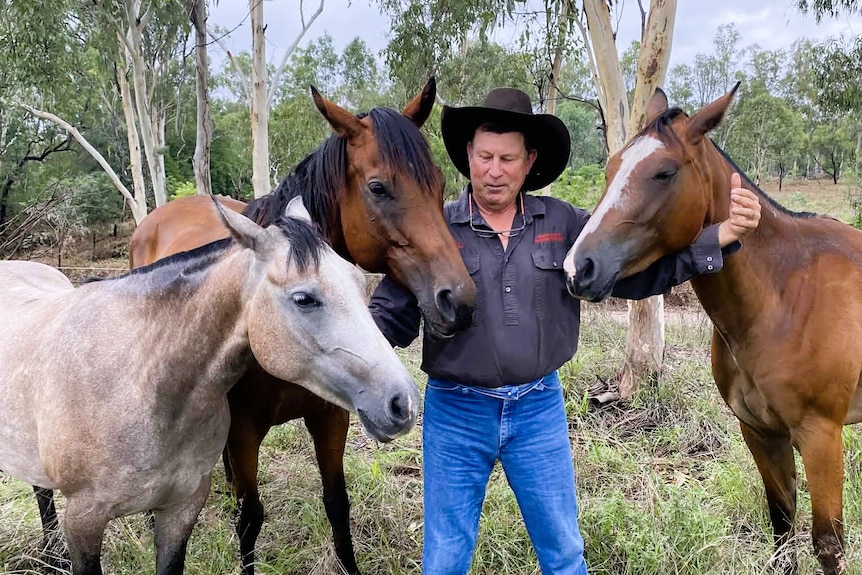 A man stands in the middle of three horses with his arms around them.
