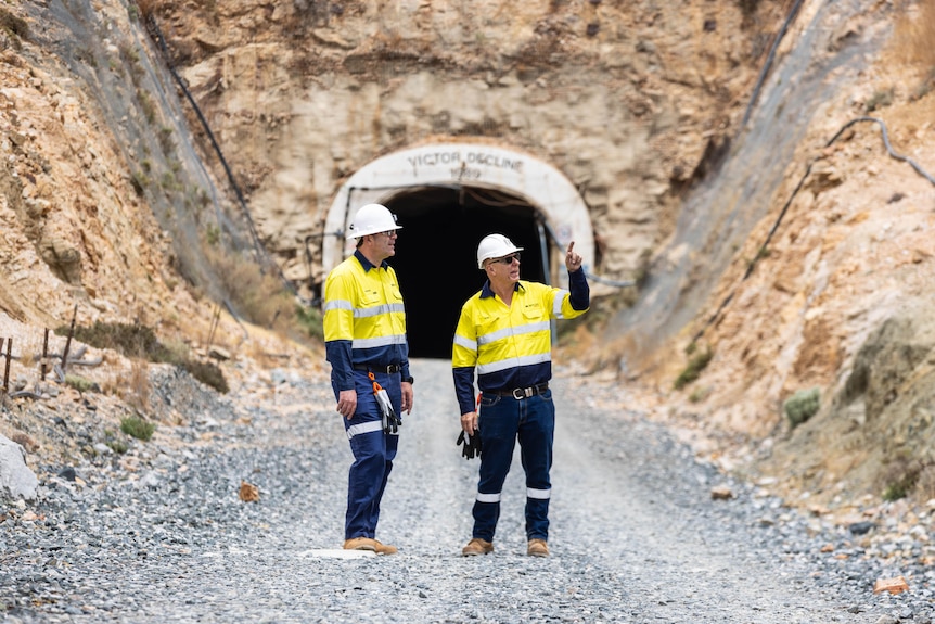 Two mine workers in high-vis and hard hats at the entrance to an underground mine.  