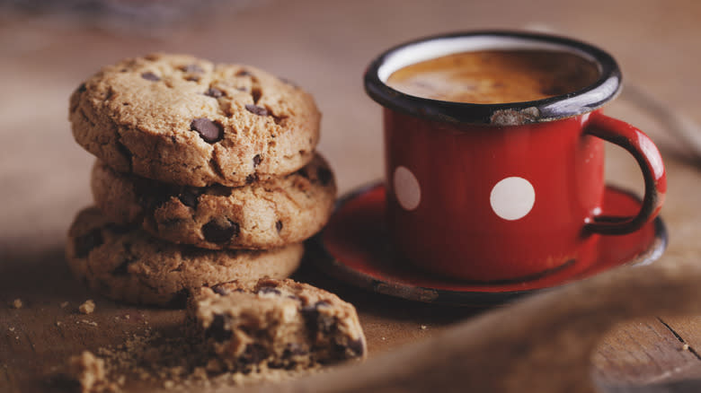 Stack of gluten-free chocolate chip cookies on wooden table beside mug of hot chocolate
