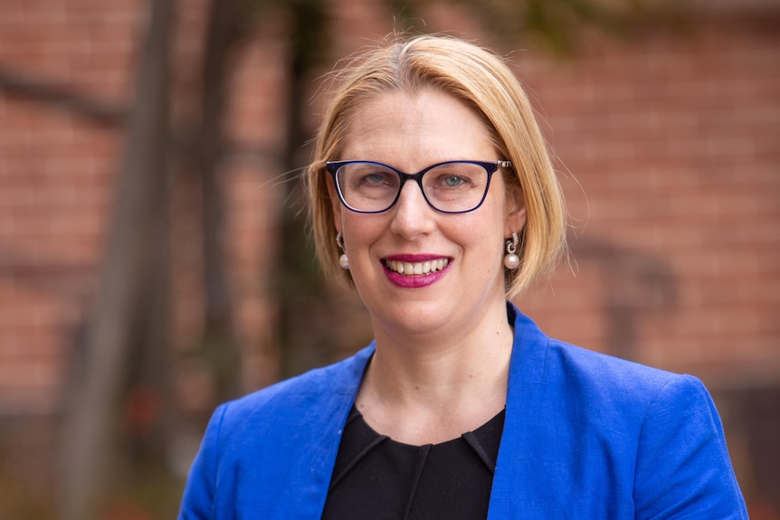 A woman wearing glasses, a black top, and a cobalt blue blazer