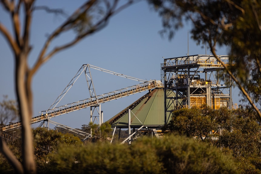 An idle processing plant framed between trees in bushland.   