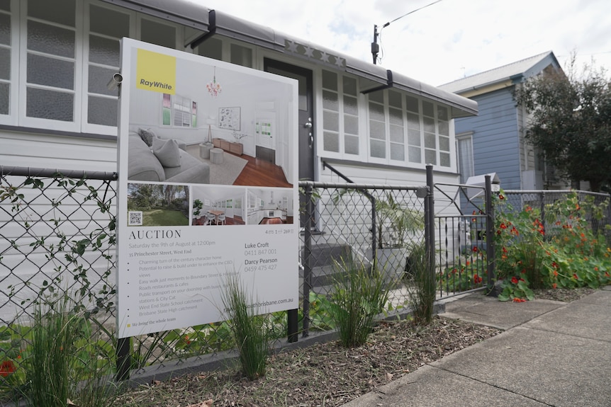 A house with a wire fence and a auction sign out the front.