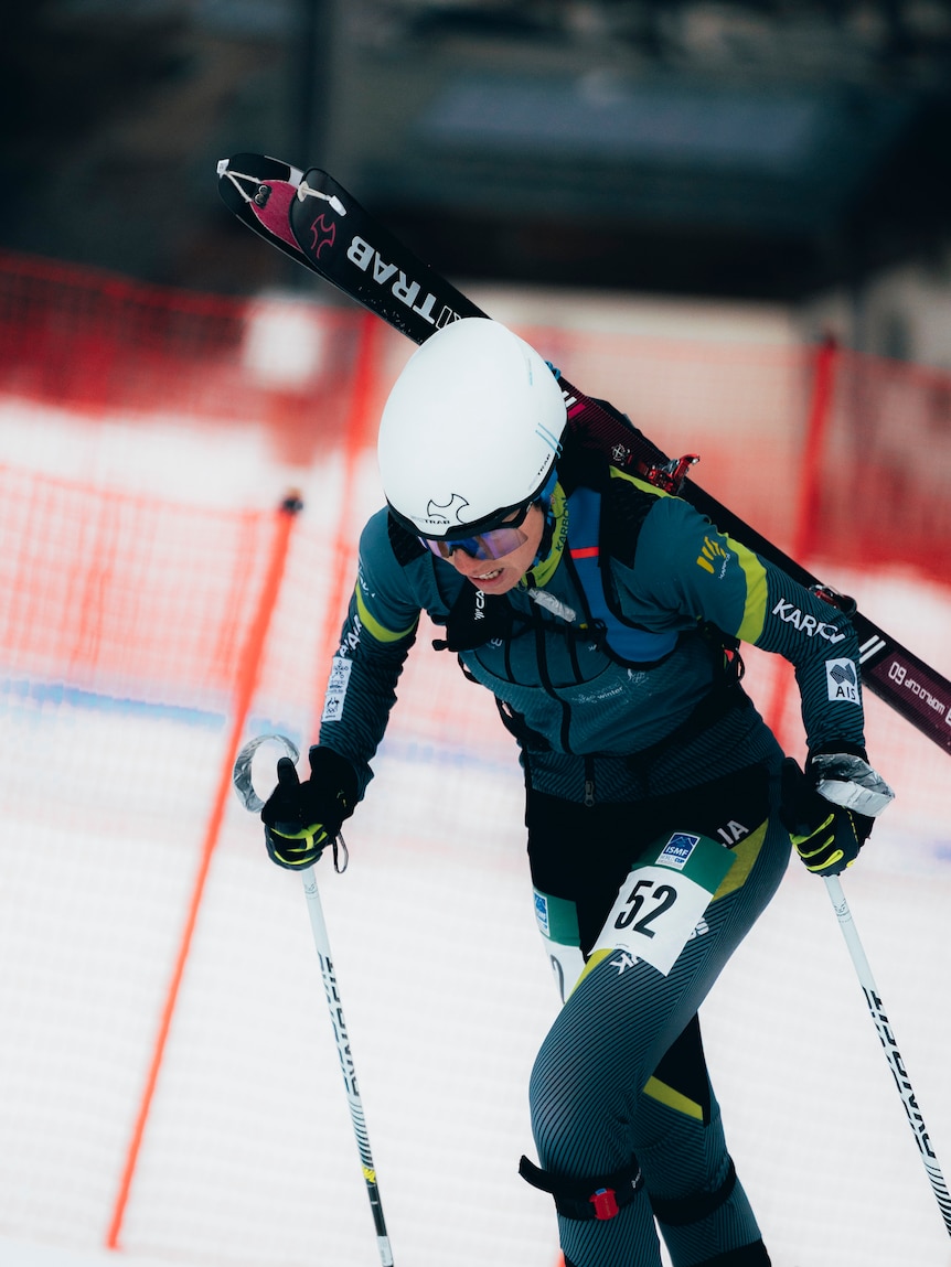 A female ski mountaineering athlete is climbing up a mountain. 