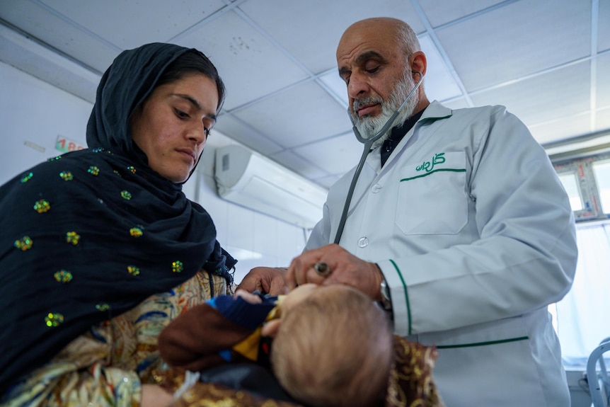 An Afghan doctor listens to the heartbeat of a baby, while the child's mother looks on.