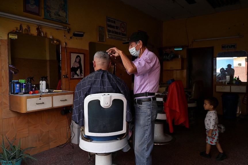 A man wearing a medical mask cuts another man's hair.
