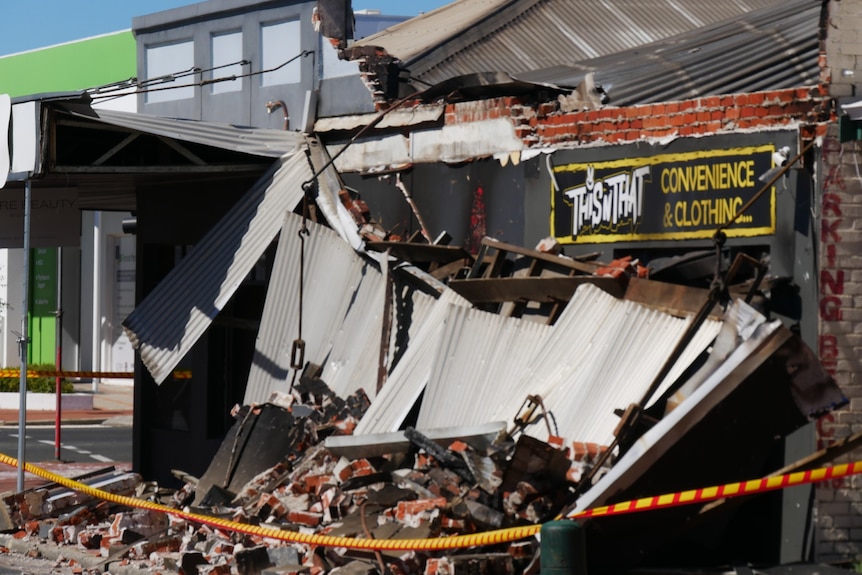 Mangled tin atop a pile of rubble lying in front of a small shop thaat has been firebombed.