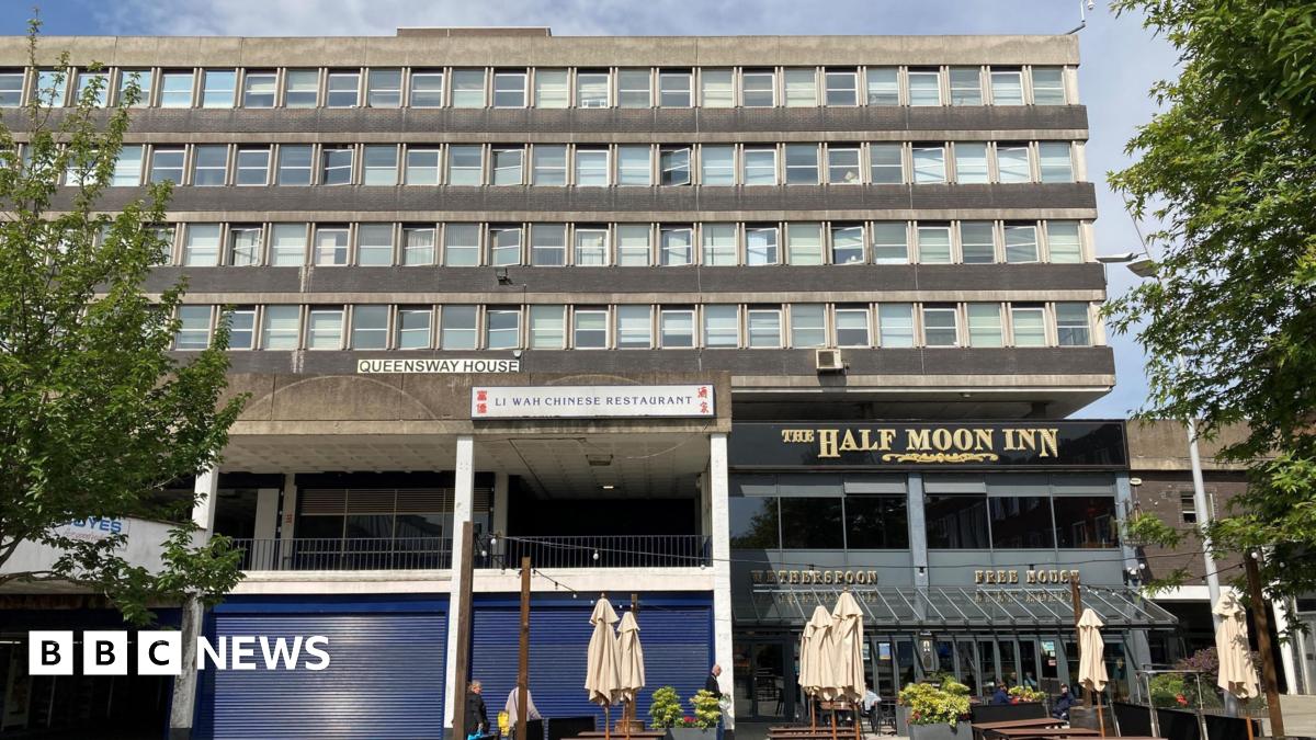 West Precinct is a large, concrete Brutalist-style building. Pictured are two businesses at the base of the block - the Half Moon Inn and a Chinese restaurant with its blue shutters down.