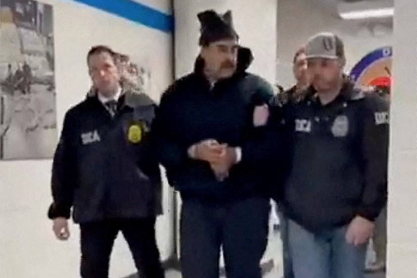 Handcuffed Maduro in dark tracksuit and beanie marched by officers down a hallway