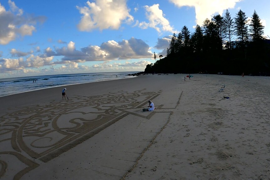 A wide shot showing people on the beach and art scratchings in the sand.