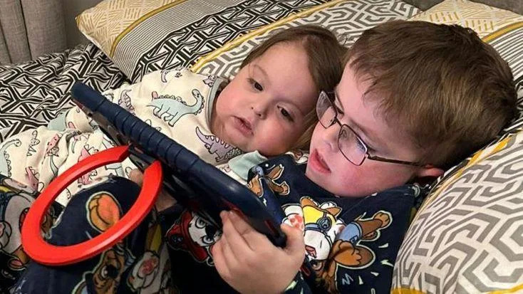 A young boy and girl and lying on a bed reading a tablet.