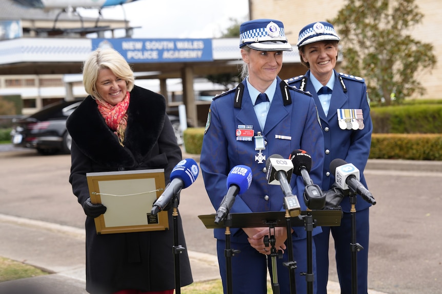 Amy Scott wearing a police uniform in front of microphones, in front of Premier, Police Commissioner and Police Minister