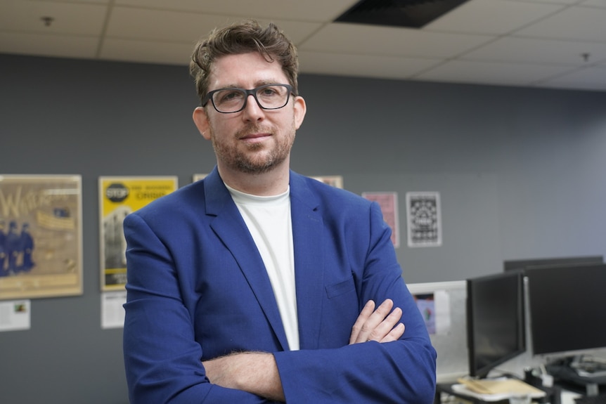 Man stands with arms crossed looking into camera.