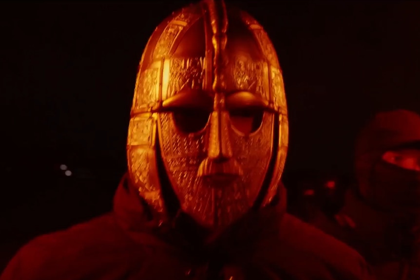 Guy wears a janky wooden mask.